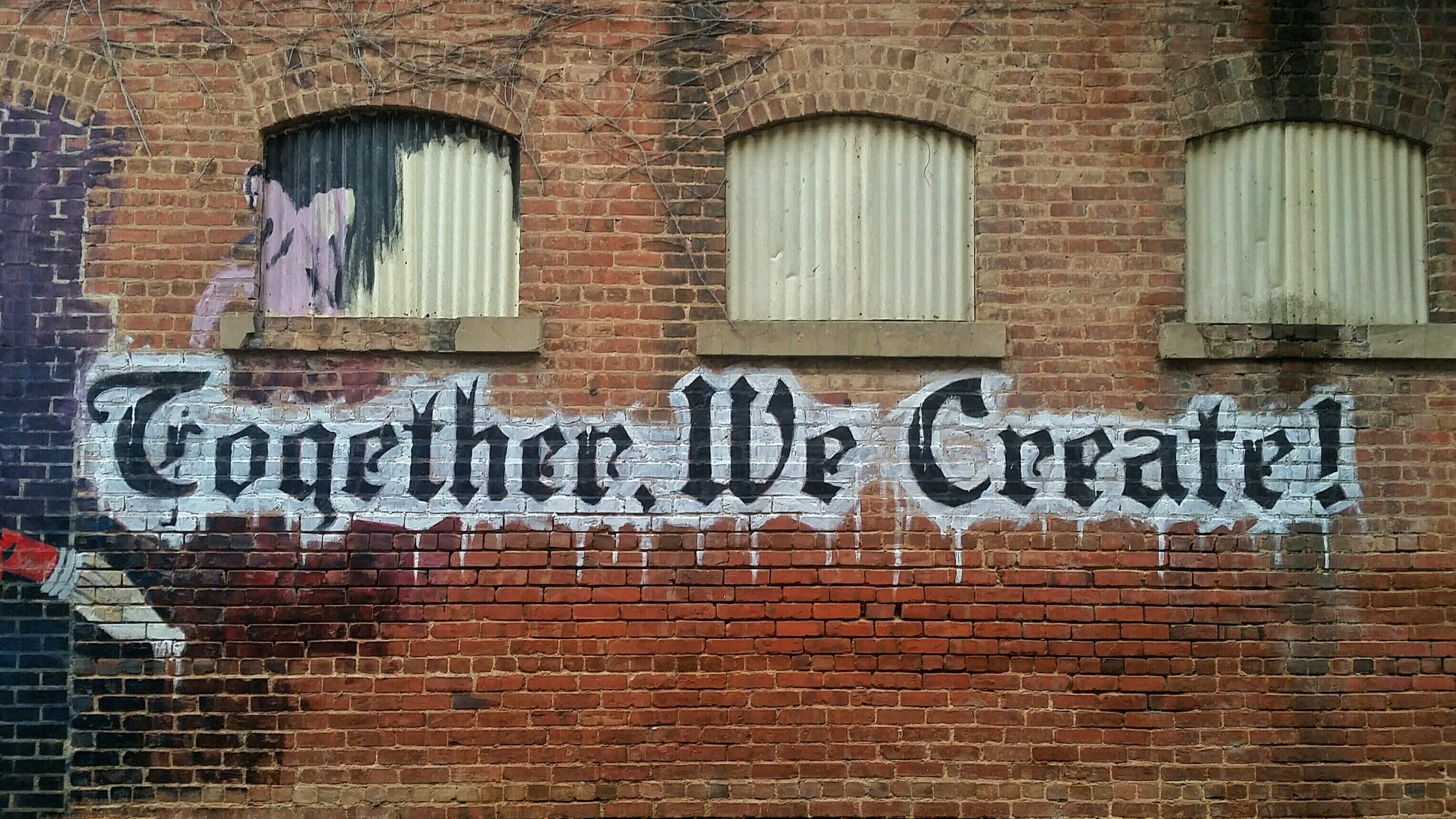 brick wall with together we create painted on it